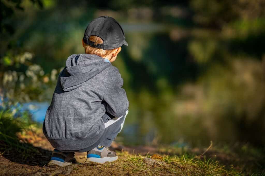 Young boy crouching by a river, observing the water carefully.