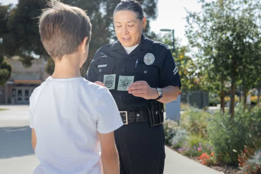 Police officer speaking with a young boy outdoors in a park setting.